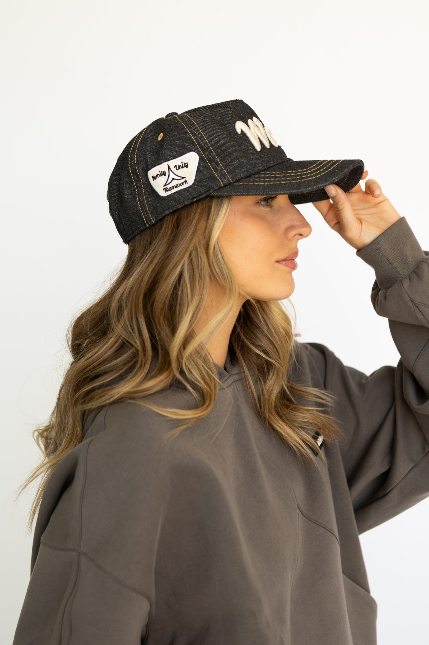 Woman wearing a dark denim cap with white text and a logo, against a plain background