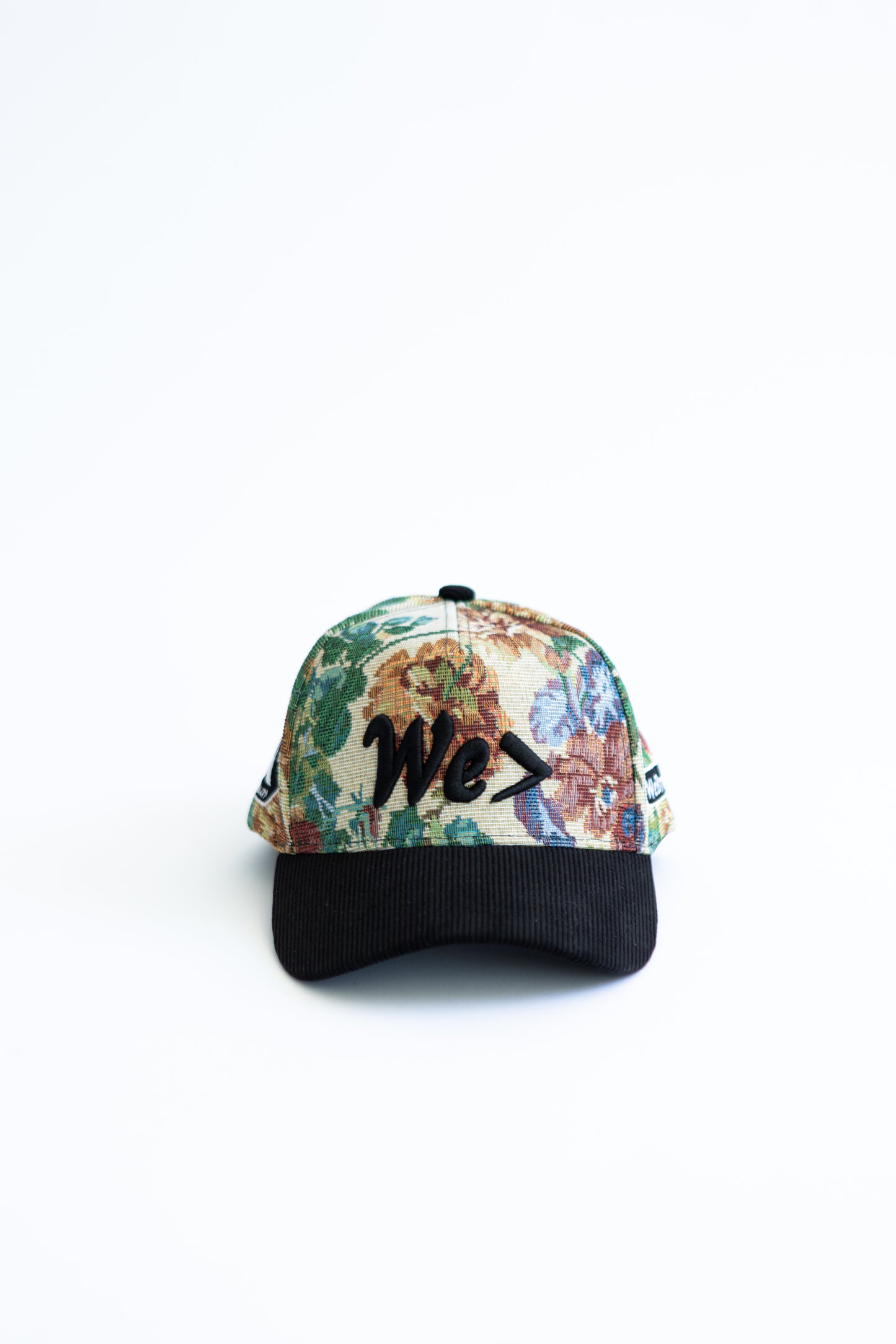 Floral-patterned cap with black brim and 'WE>' logo on a white background