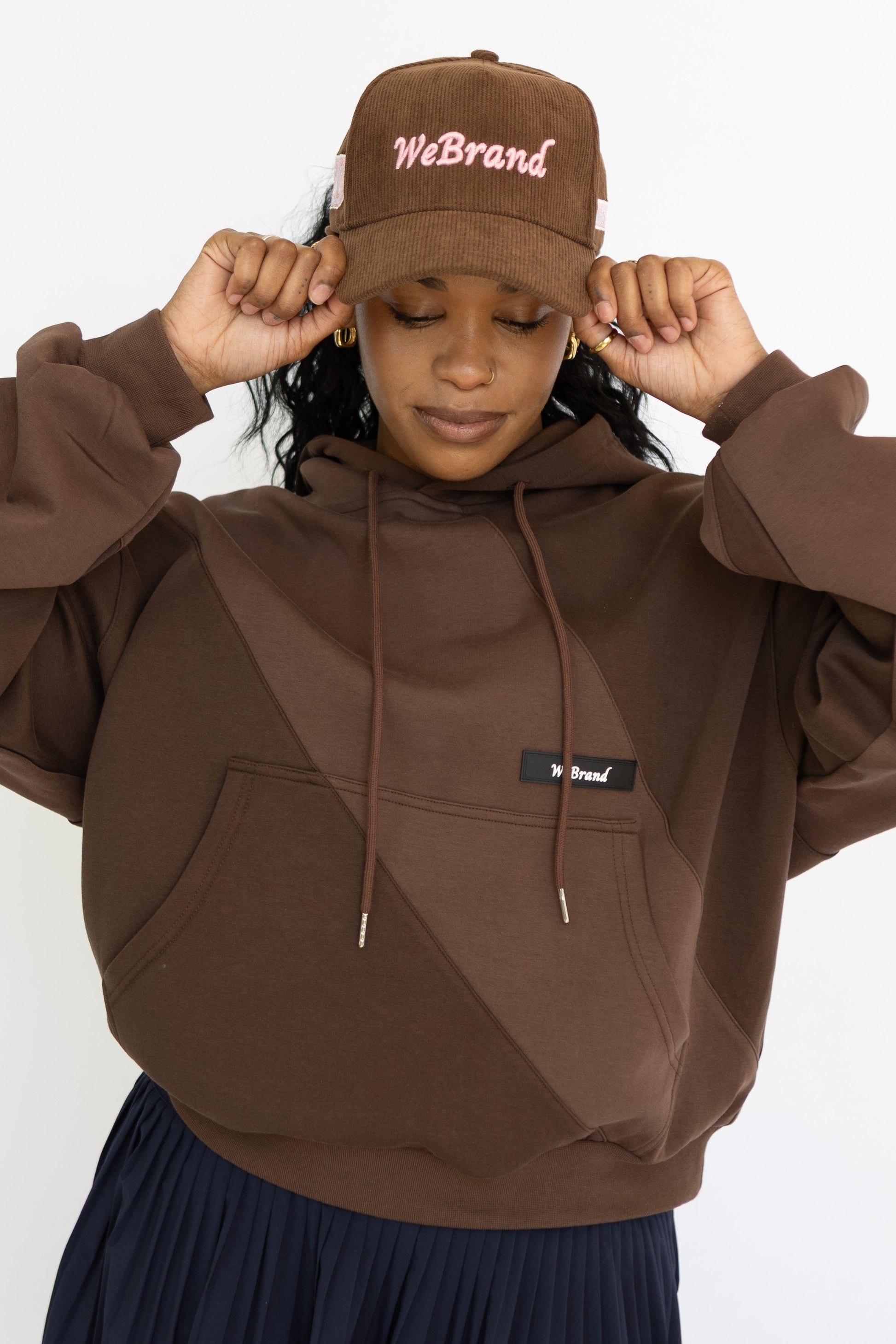 Person wearing a brown hoodie and navy skirt with a matching cap on a white background
