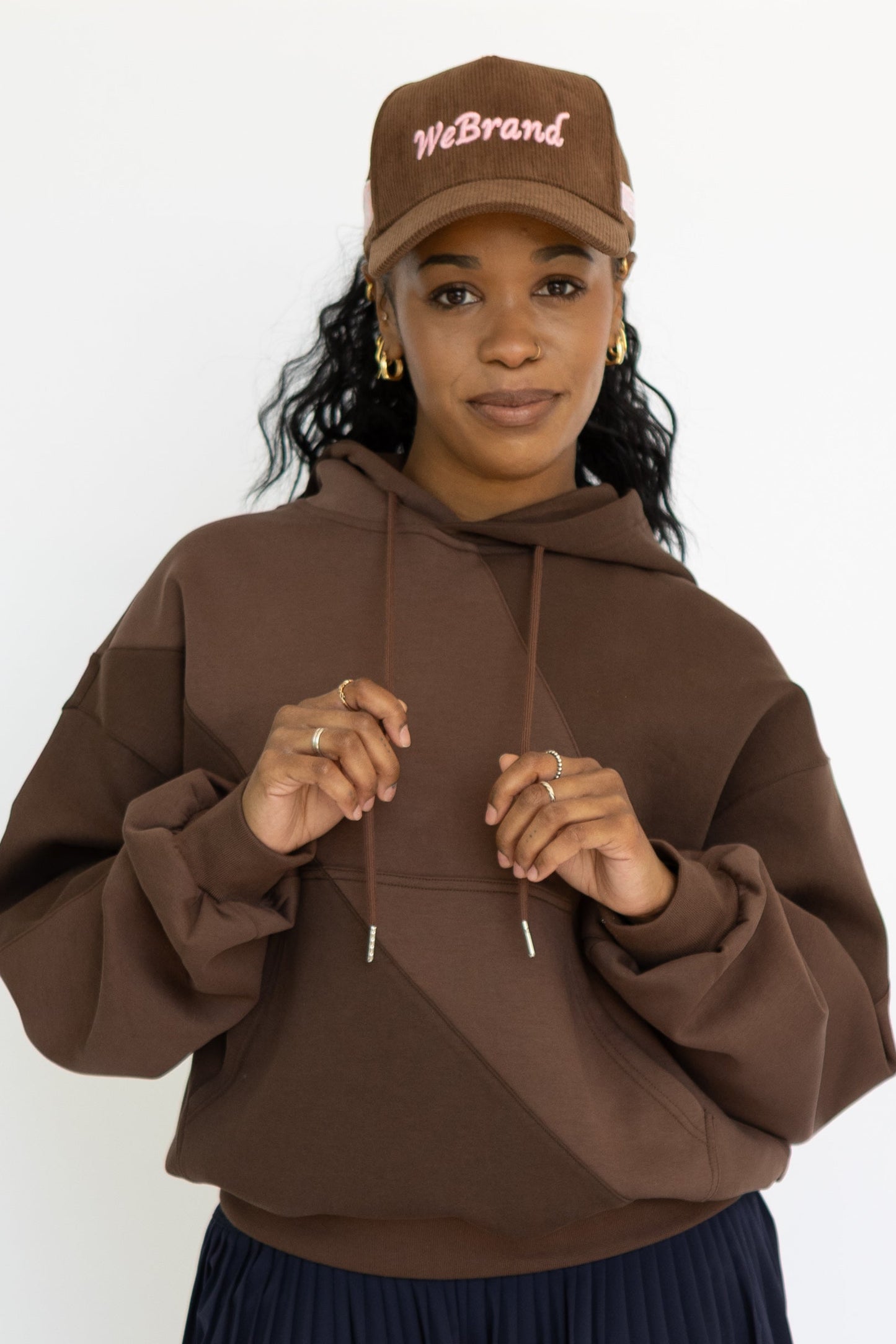 Person wearing a brown hoodie, black skirt, and colorful sneakers on a white background