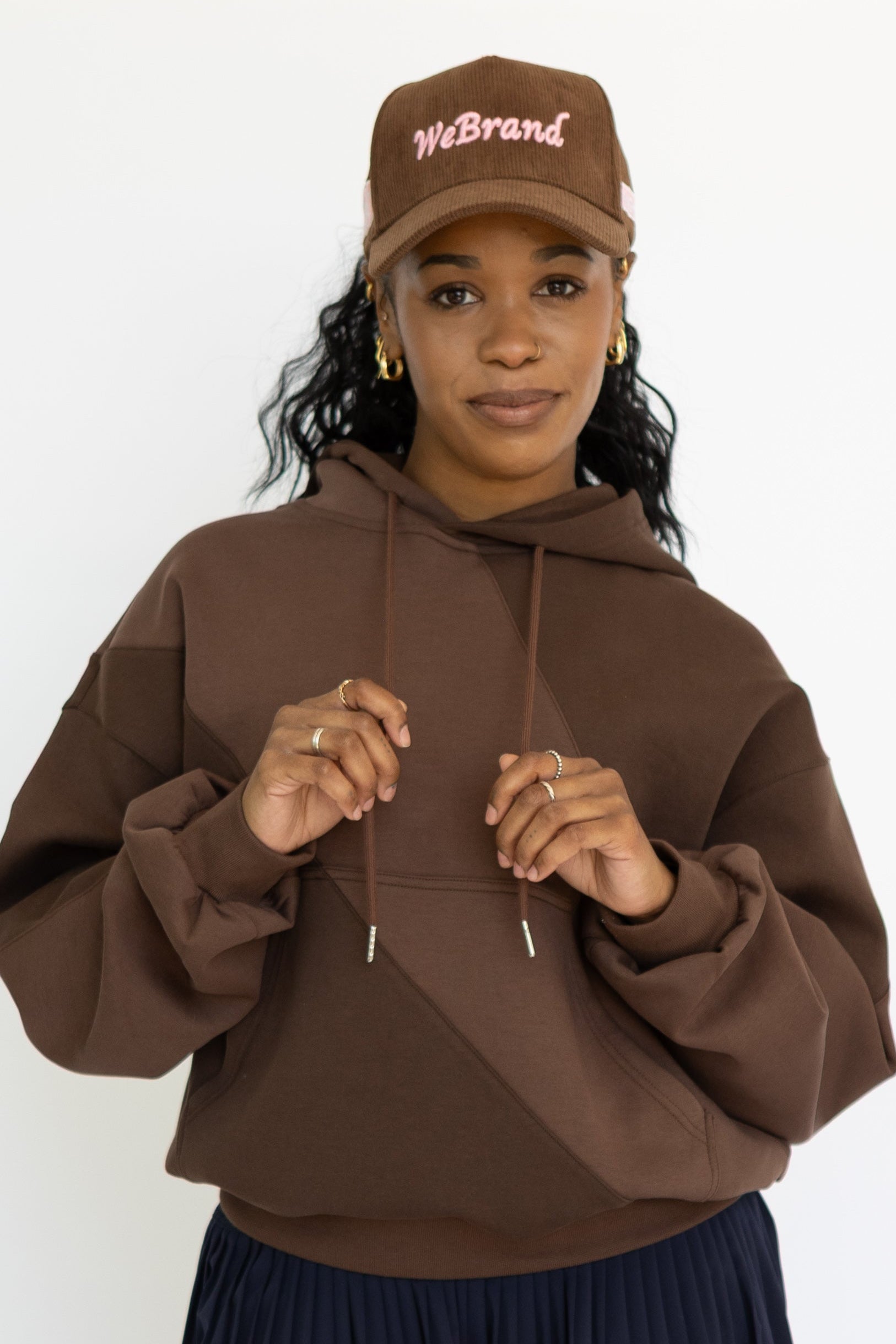 Person wearing a brown hoodie, black skirt, and colorful sneakers on a white background