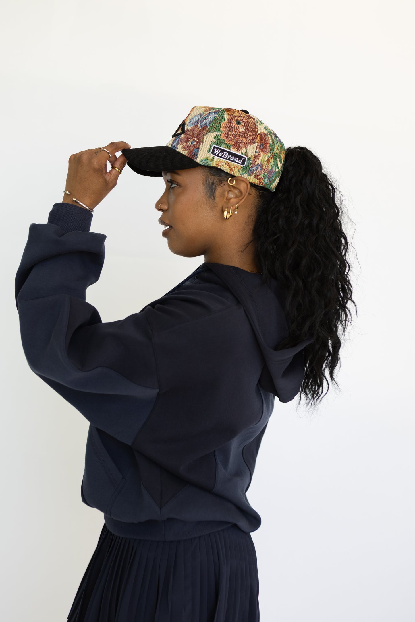Person wearing a navy blue hoodie and floral cap against a white background