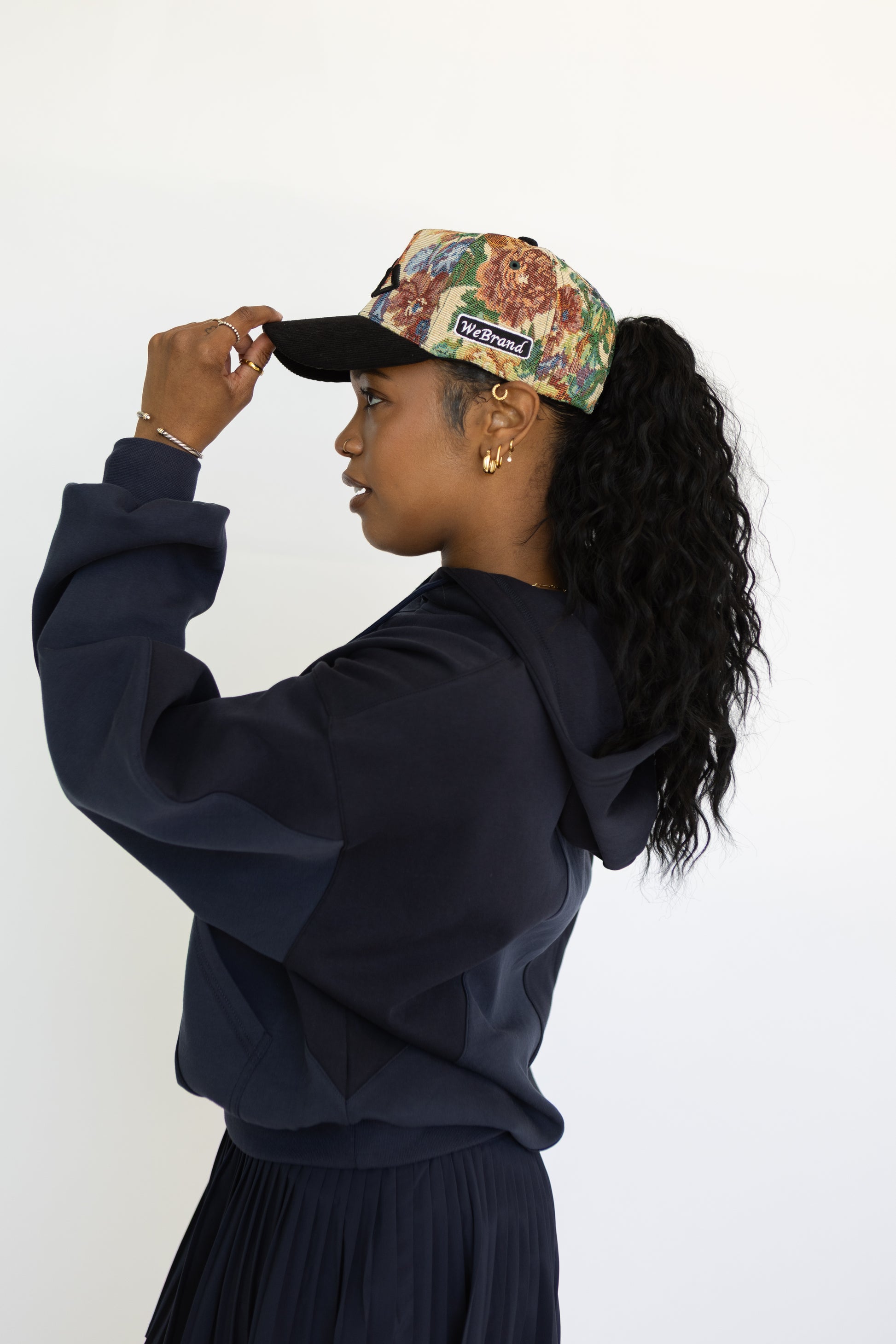 Person wearing a navy blue hoodie and floral cap against a white background