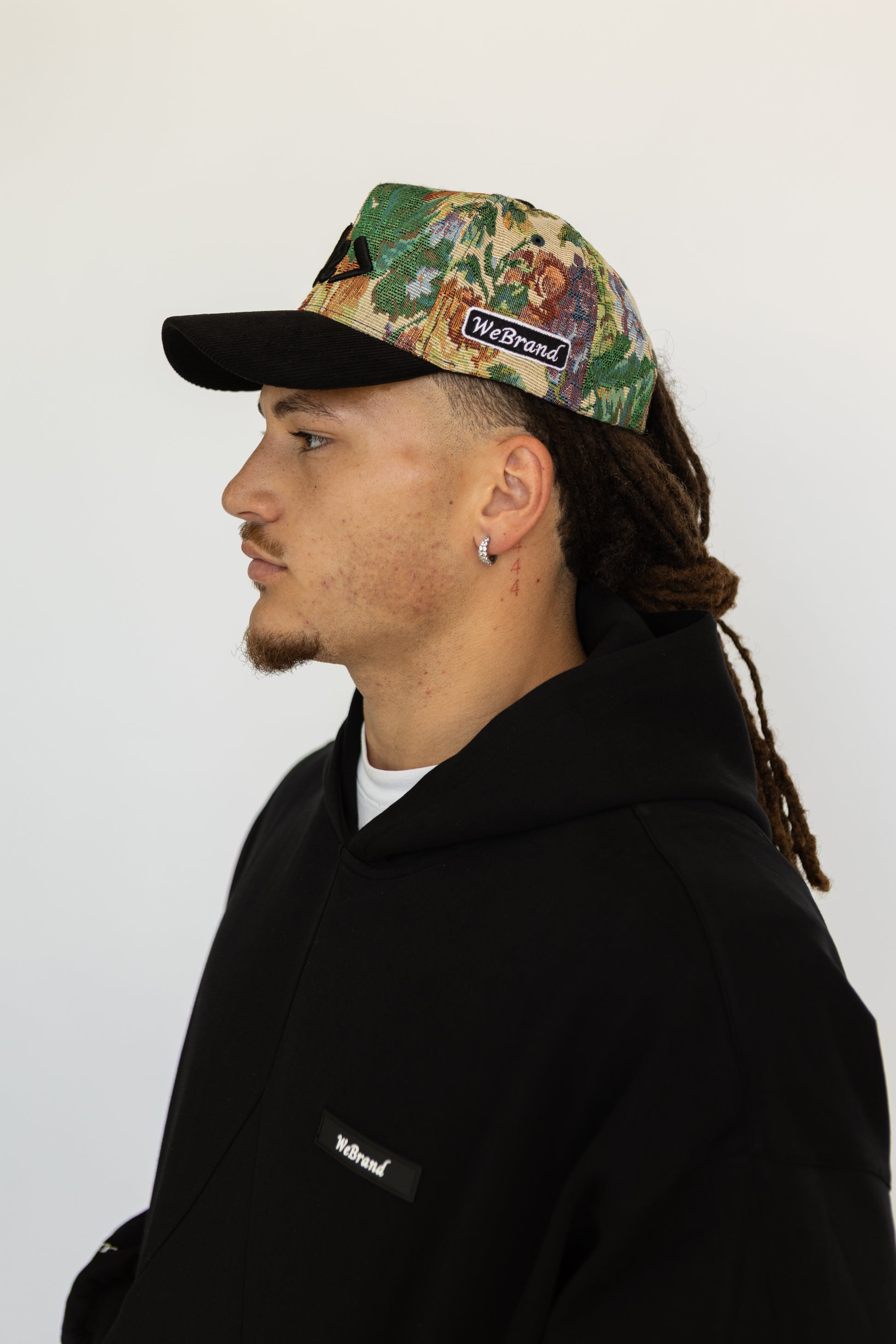 Person wearing a floral cap and black jacket with 'WeBrand' logo on a white background