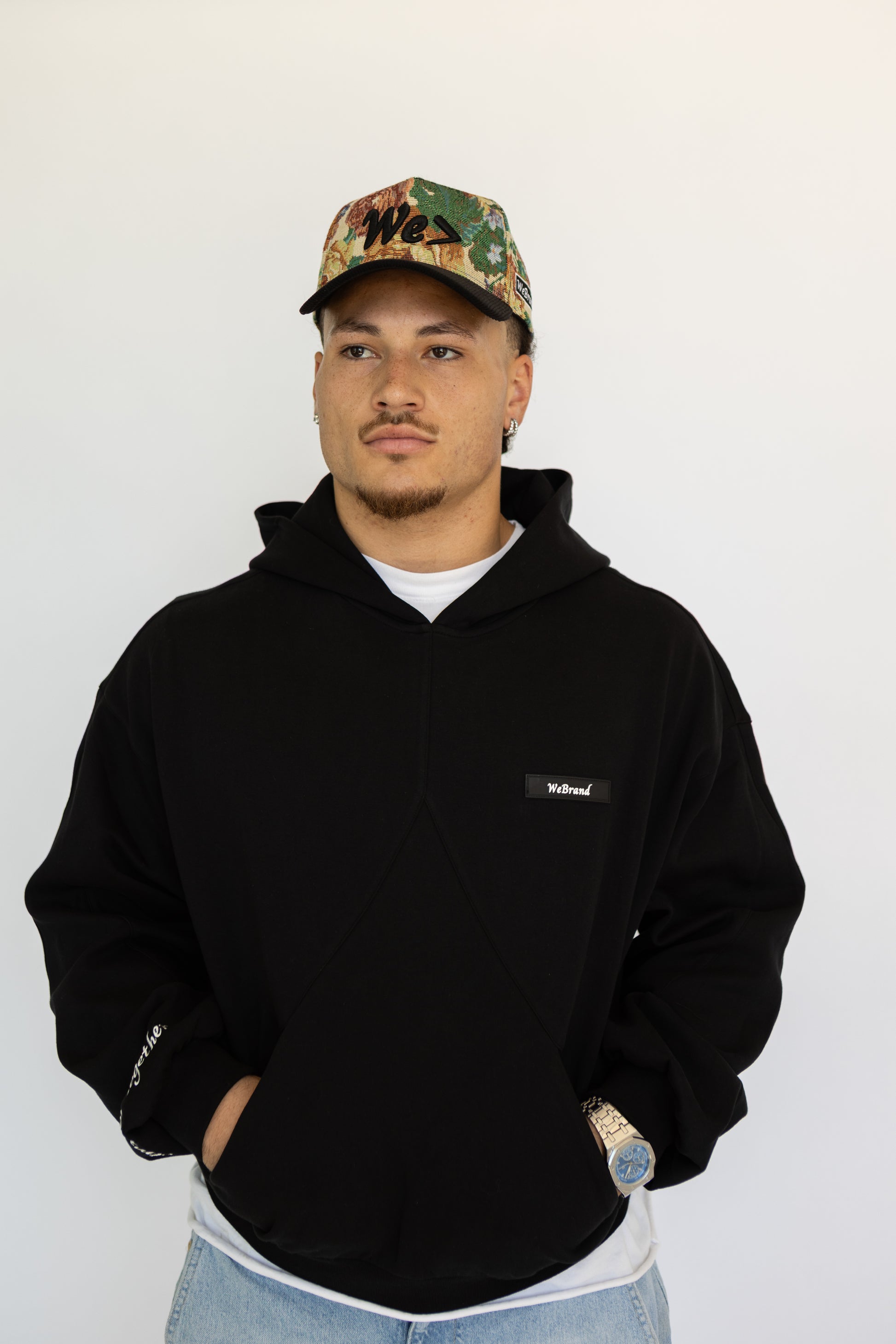 Person wearing a black hoodie and floral cap on a white background