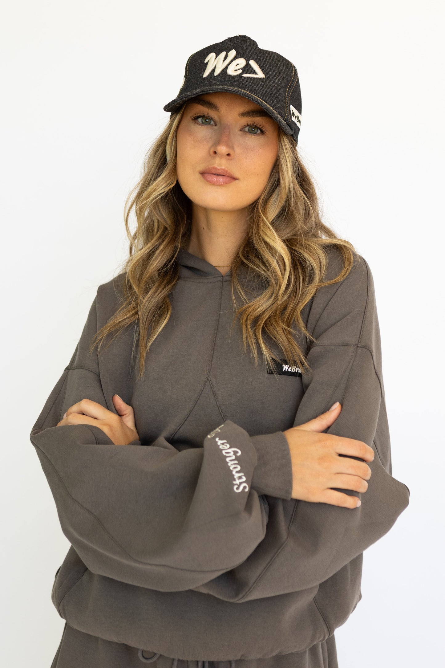 Woman wearing a gray hoodie and black cap with 'We' logo on a white background