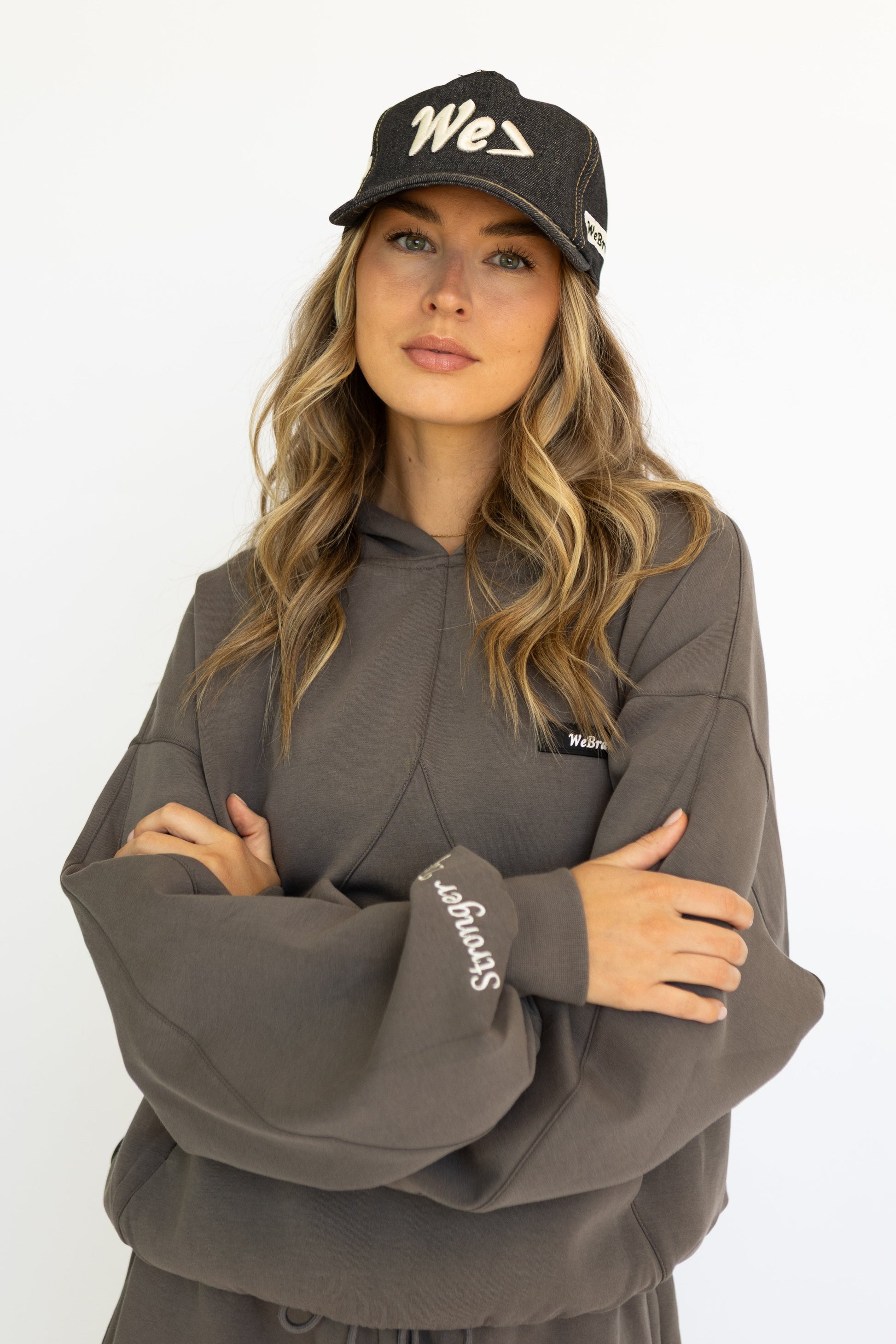 Woman wearing a gray hoodie and black cap with 'We' logo on a white background
