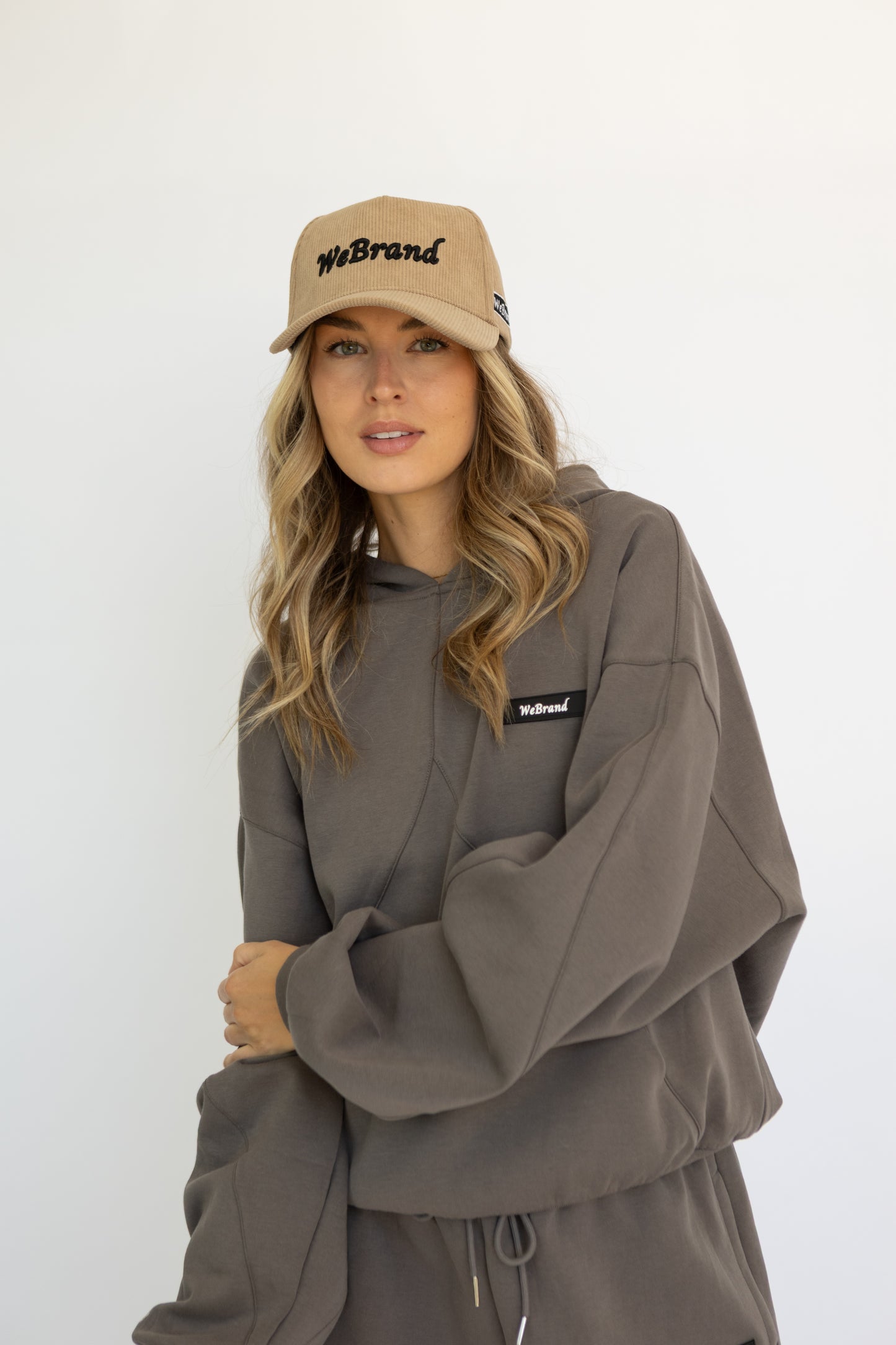 Woman wearing a gray hoodie and pants with 'WeBrand' logo, standing against a white background.