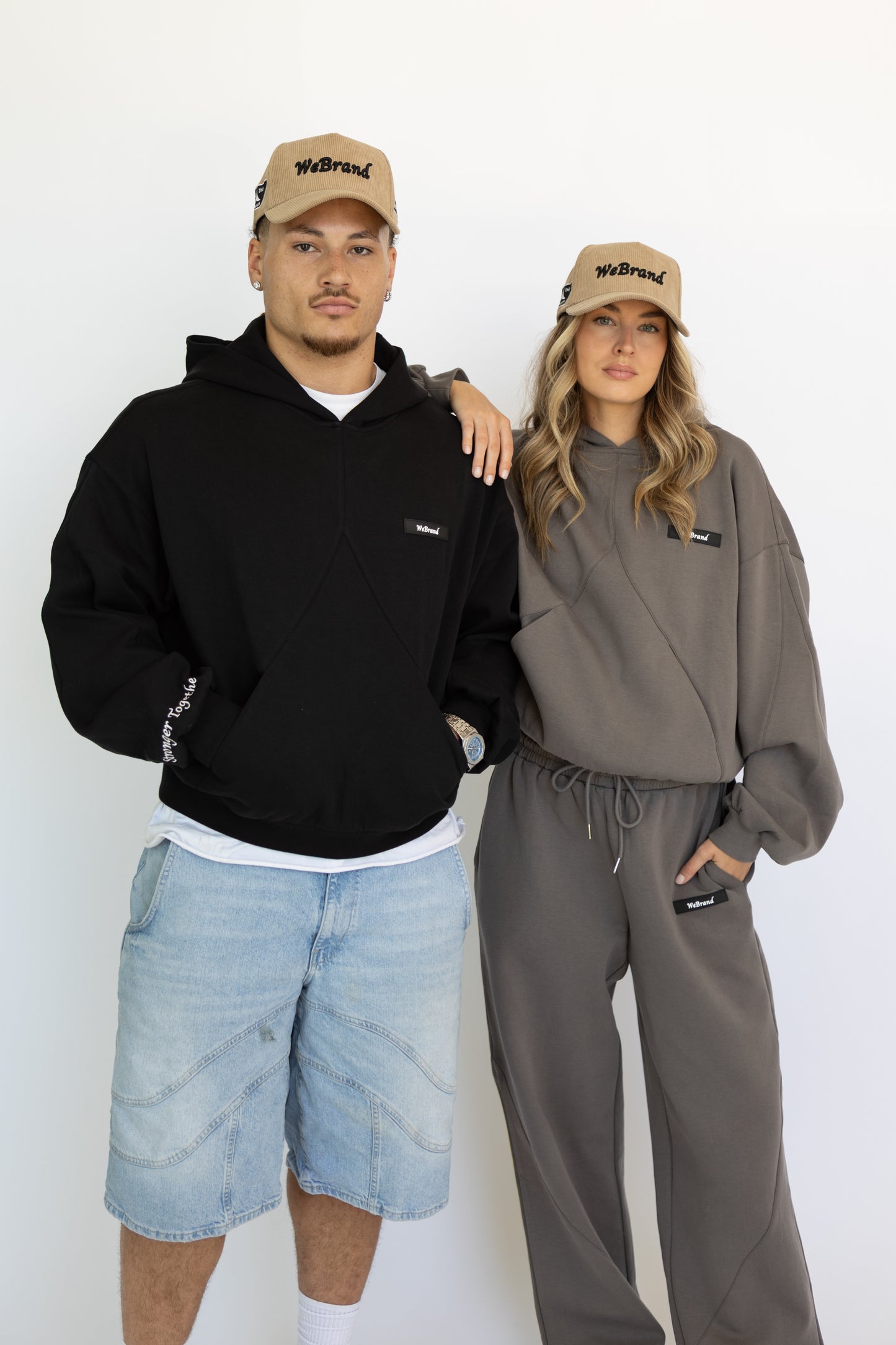Two people wearing matching black and gray outfits with 'WBrand' hats on a white background.