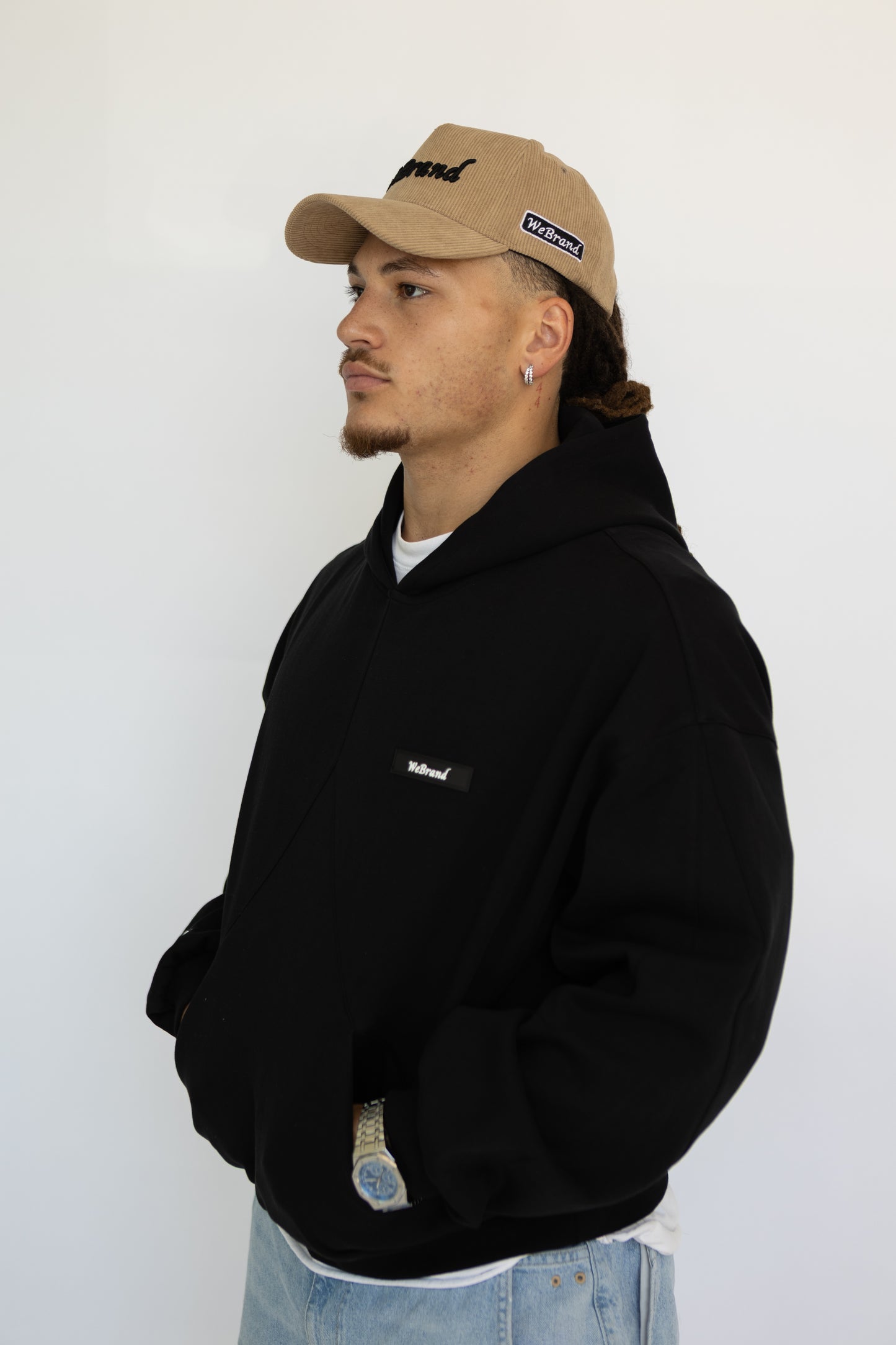 Person wearing a black hoodie and beige cap with visible branding against a white background