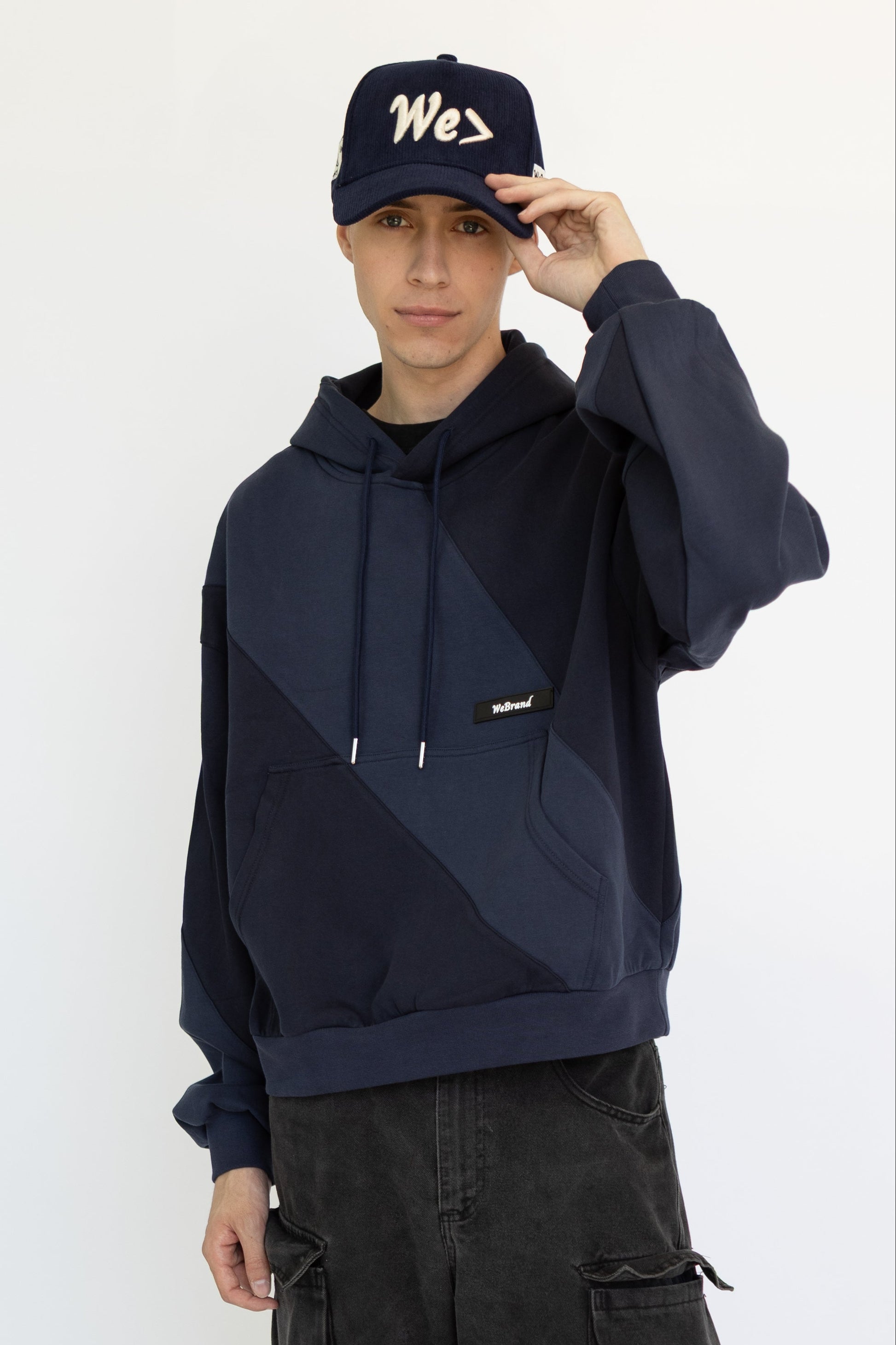 Man wearing a dark hoodie and cargo pants with a cap on a white background