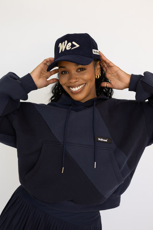 Woman wearing a navy blue hoodie and cap with 'We' text on a white background