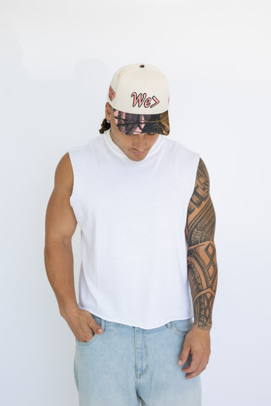 Person wearing a white sleeveless shirt, light blue jeans, and a cap with a visible brand logo on a white background.