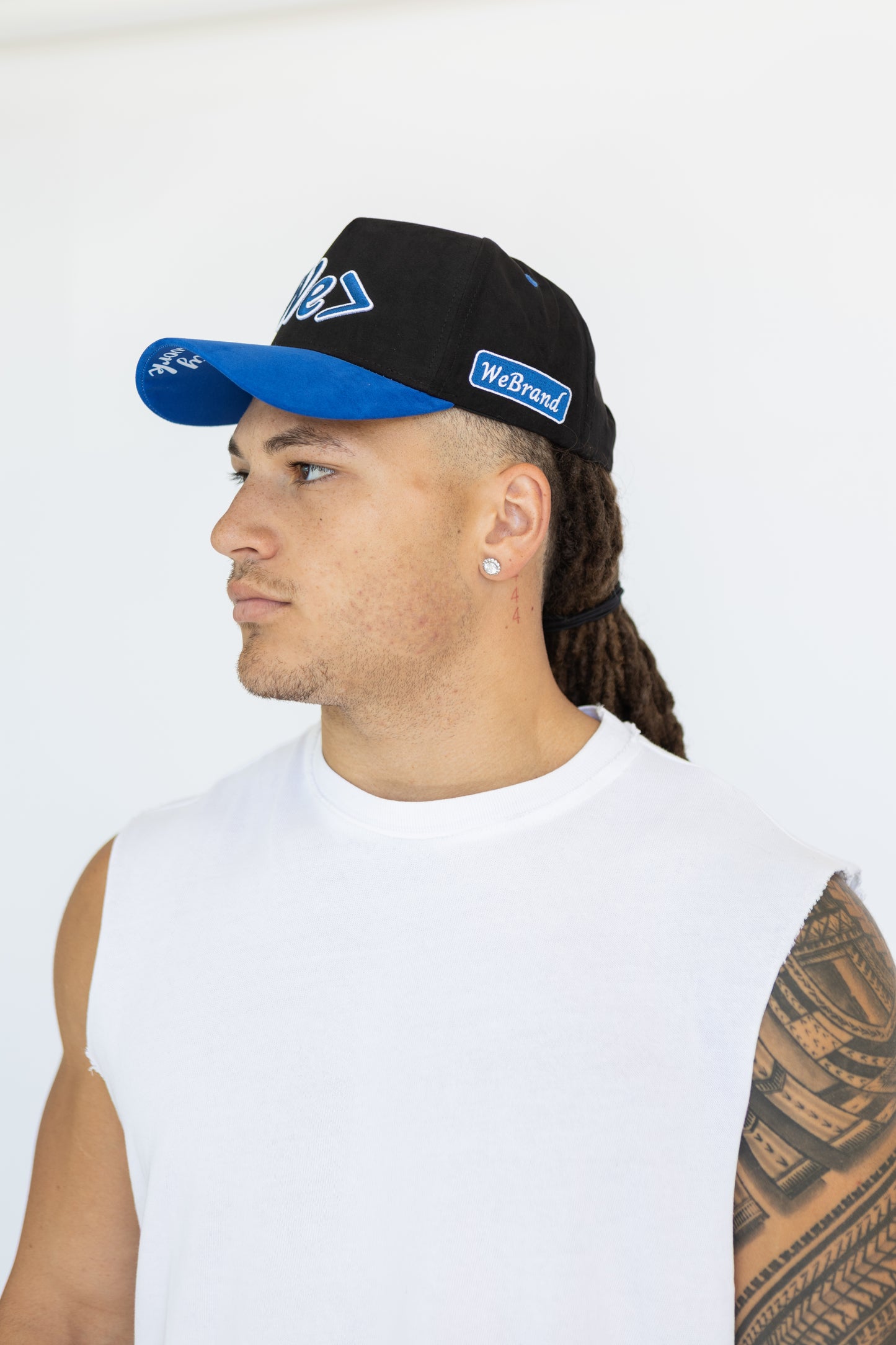 Man wearing a black cap with blue bill and visible branding on a white background