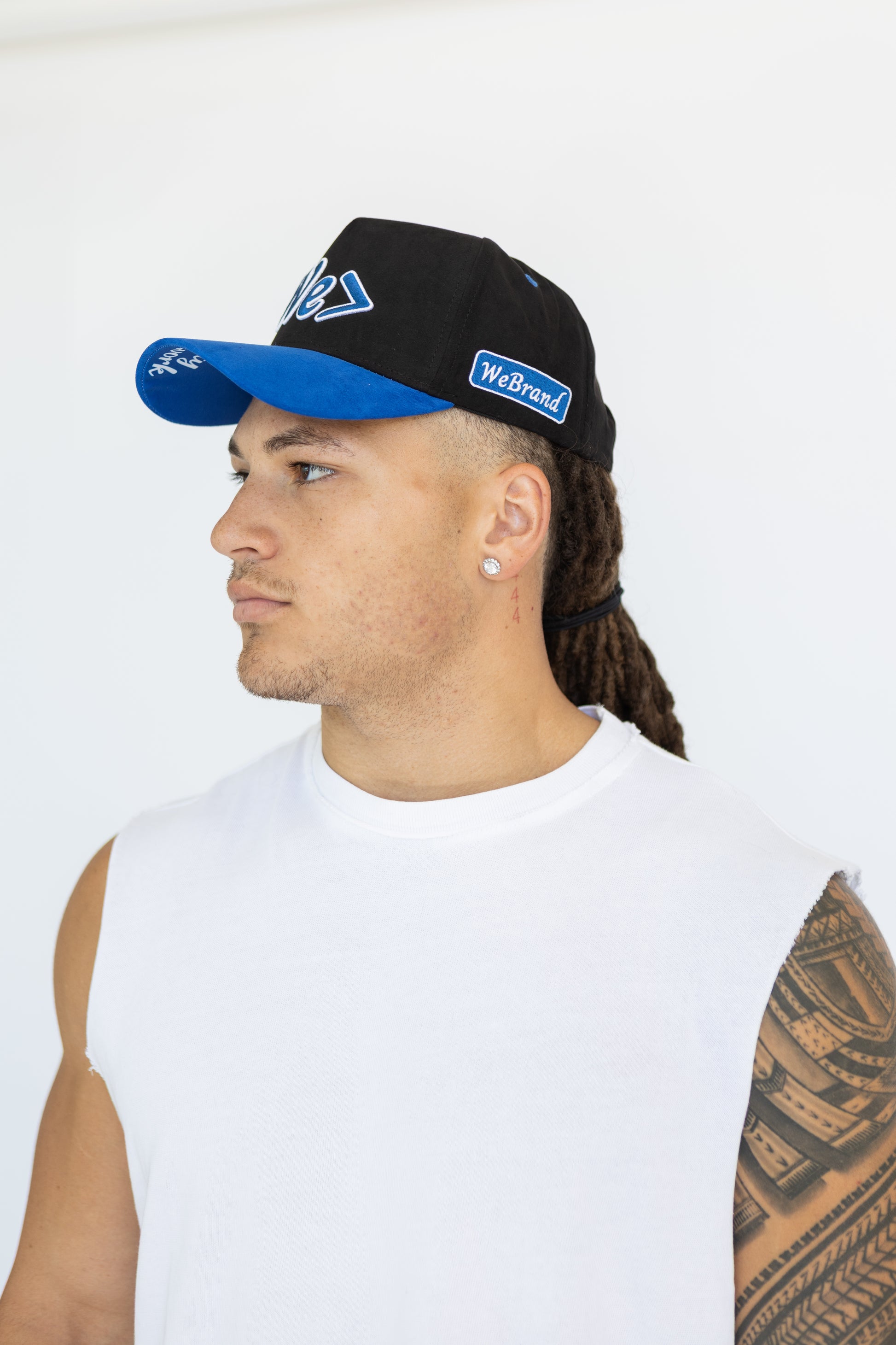 Man wearing a black cap with blue bill and visible branding on a white background