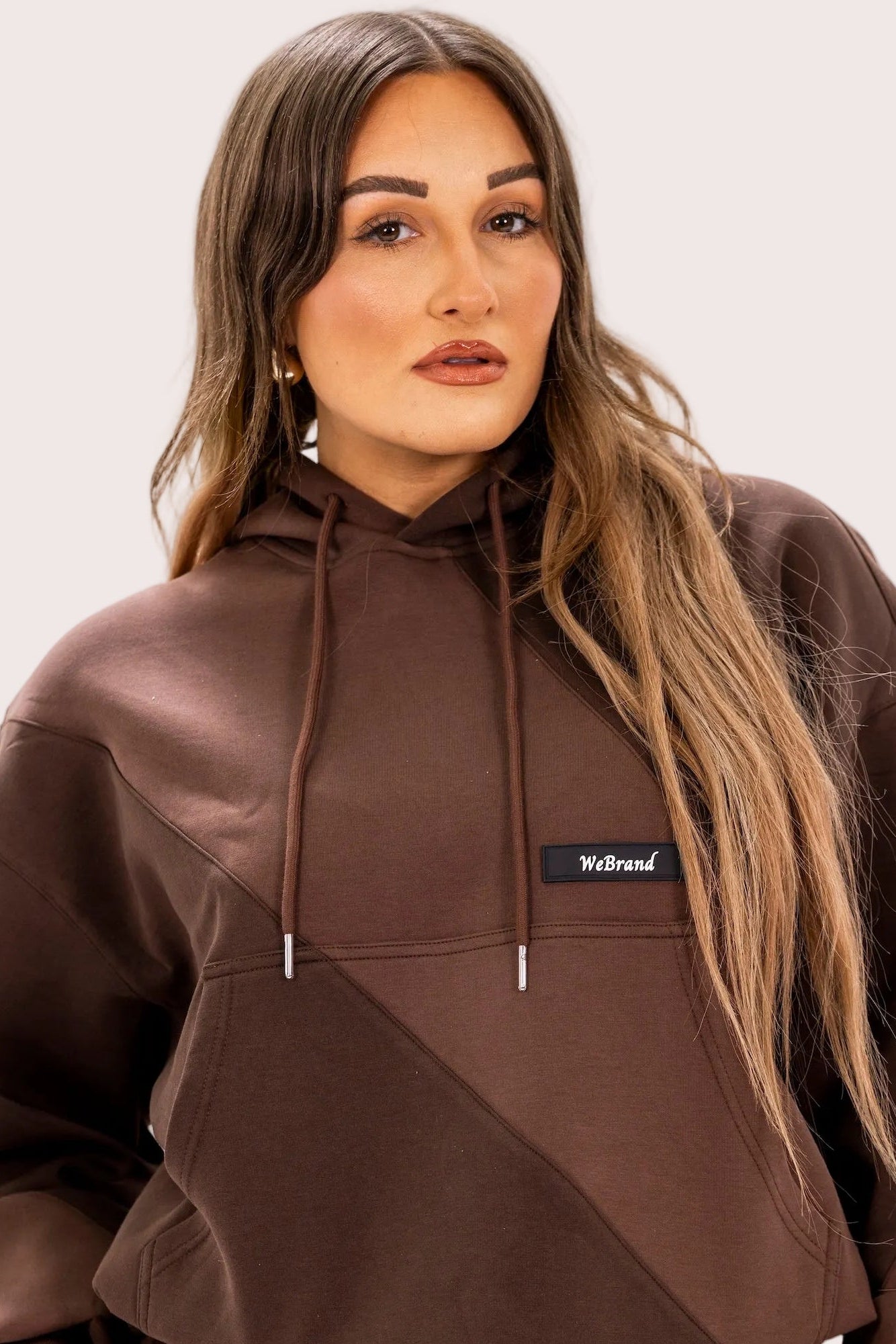 Woman wearing a brown hoodie and pants with a visible brand logo on a white background