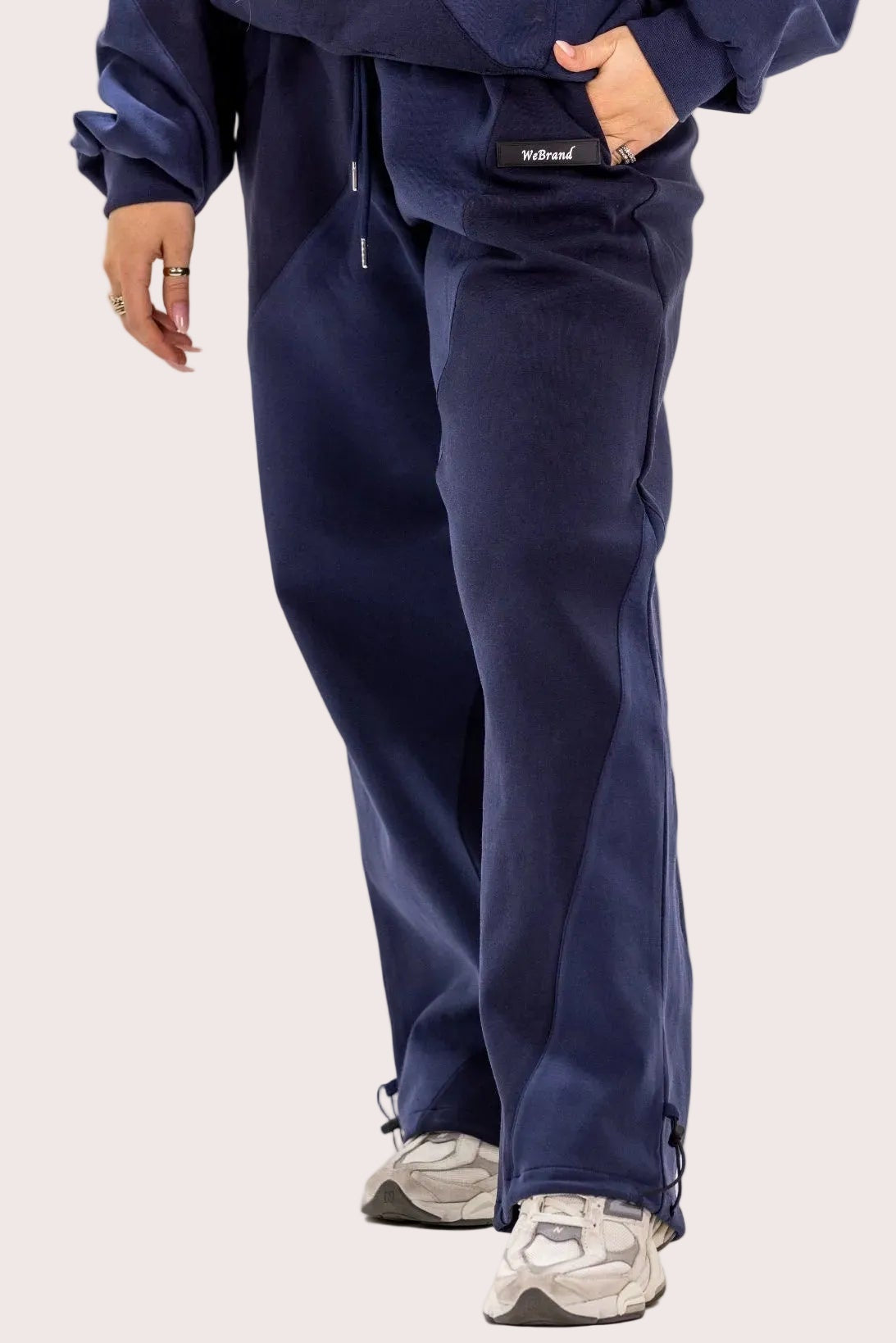 Person wearing navy blue tracksuit with white sneakers on a light beige background