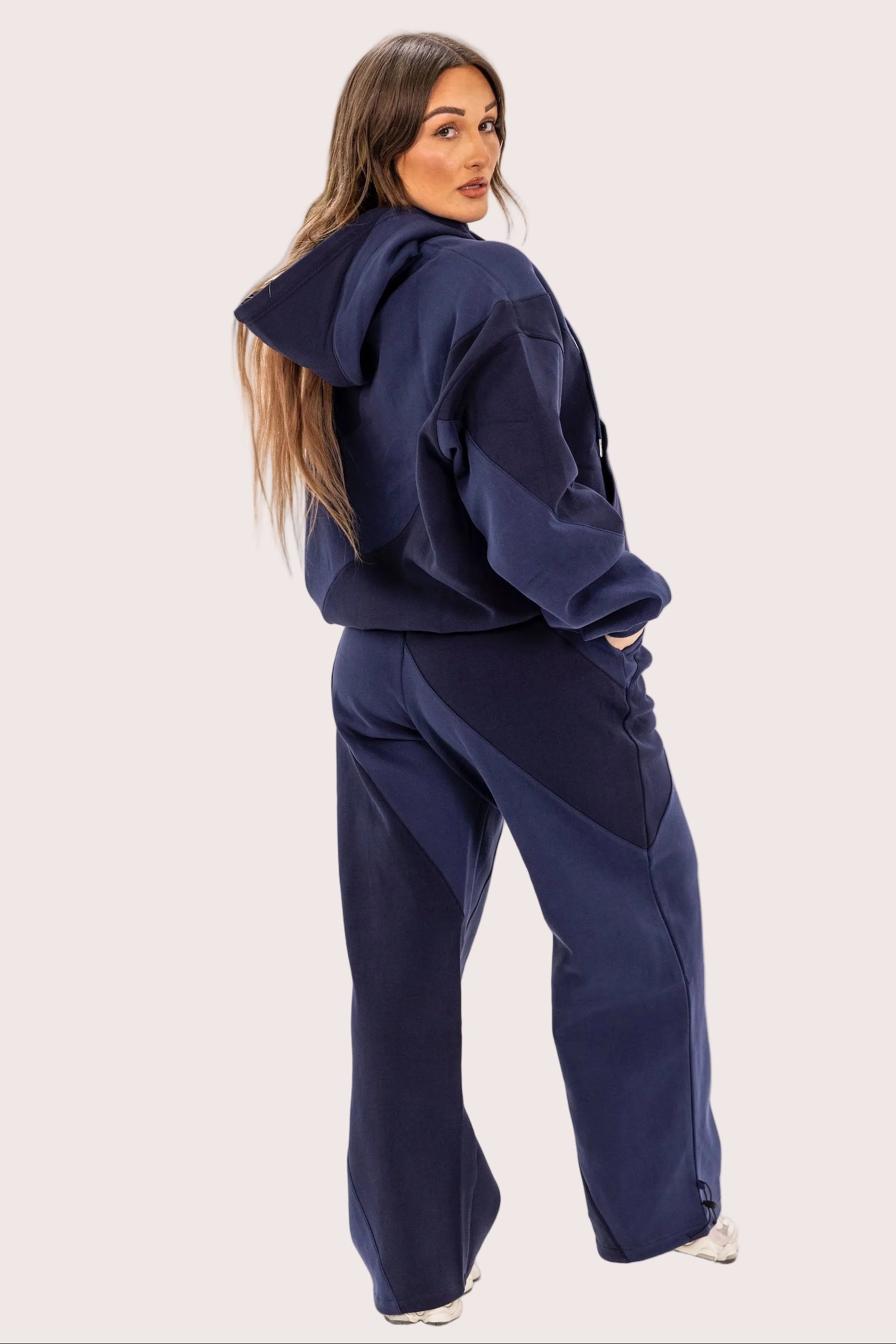 Woman wearing a navy blue tracksuit on a light pink background