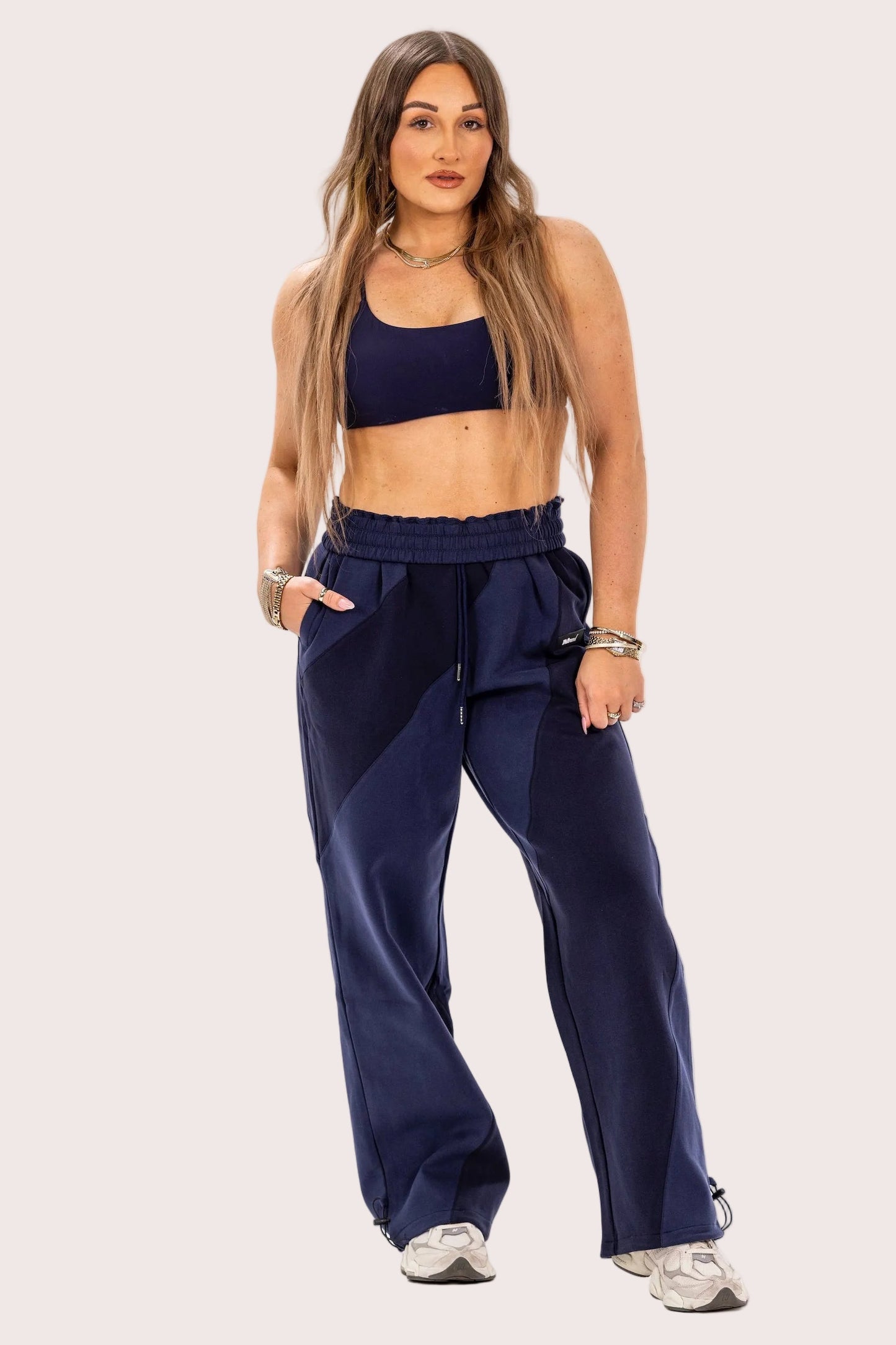 Woman wearing a navy blue sports bra and pants on a light pink background