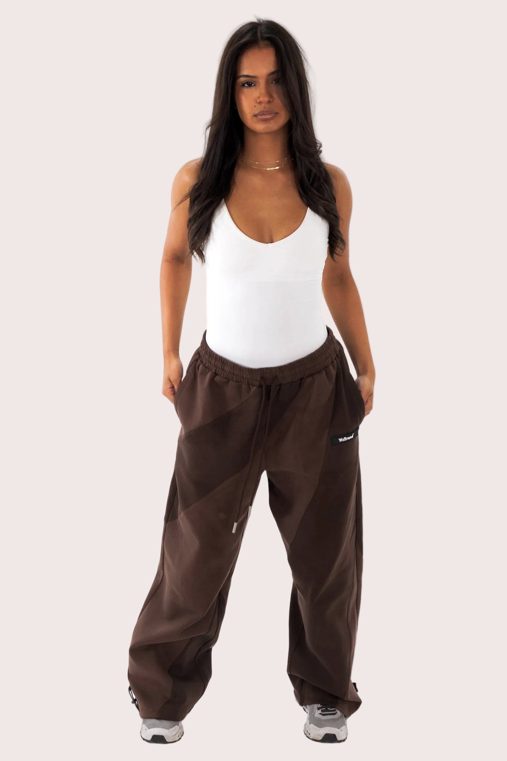 Woman wearing brown pants and a white tank top on a white background