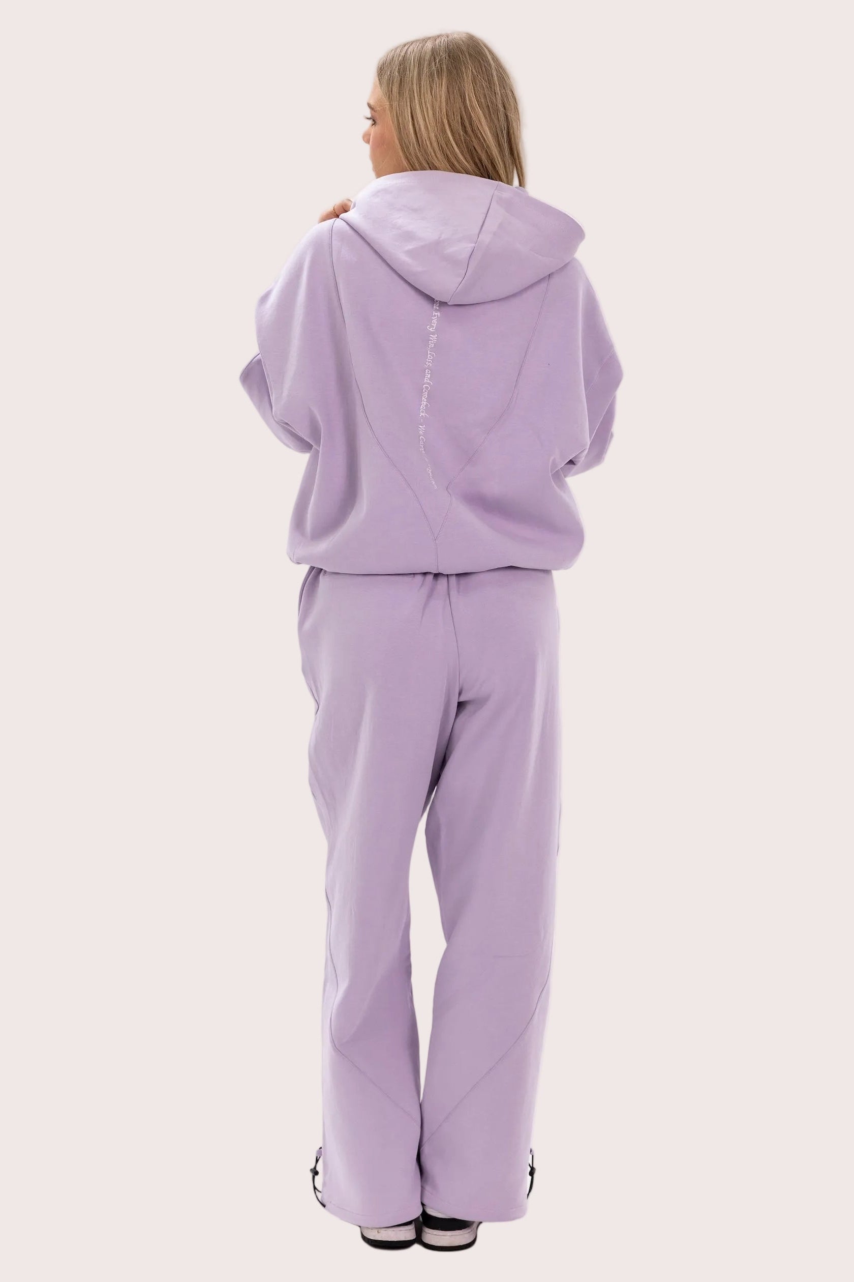 Person wearing a lavender tracksuit on a light pink background