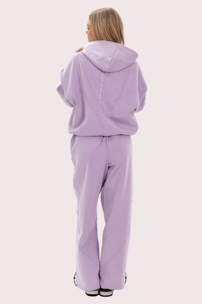 Person wearing a lavender tracksuit on a light pink background